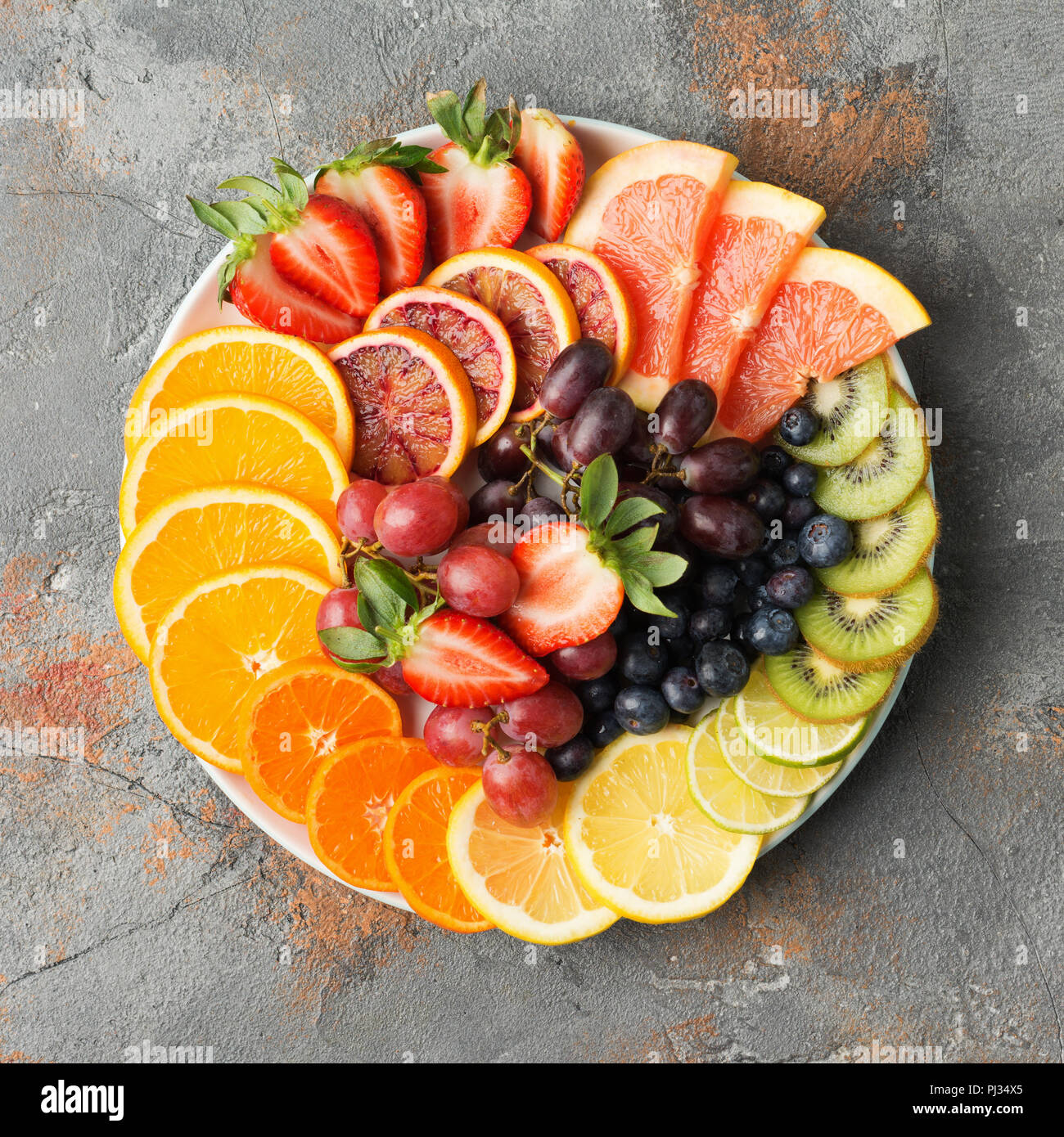 Assortiment de fruits coupés en couleurs arc-en-ciel raisins oranges fraises kiwis mangue pamplemousses sur les bleuets la table de béton gris, copiez l'espace, vue d'en haut, carré, selective focus Banque D'Images