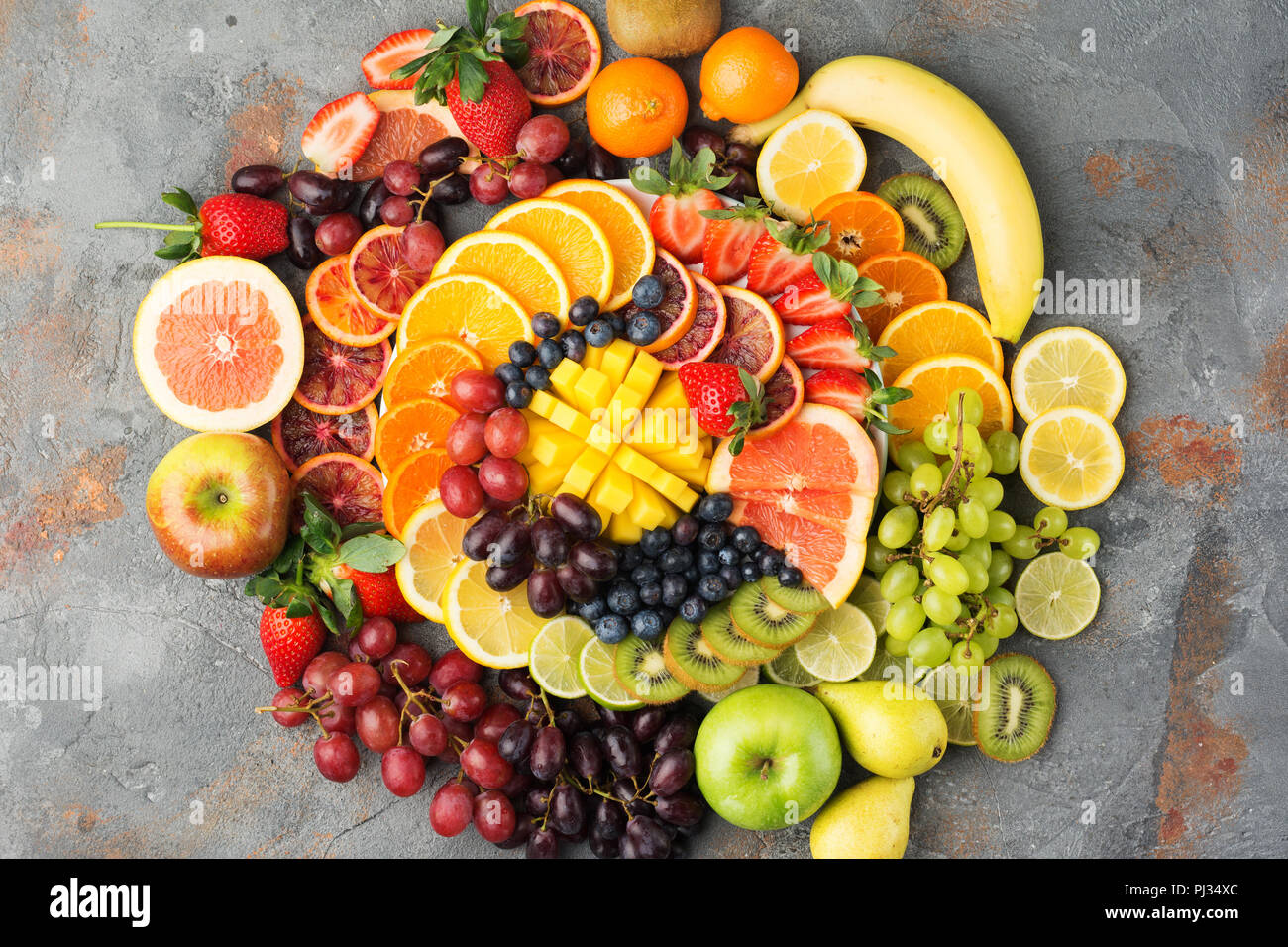 Les fruits sains en arrière-plan des couleurs arc-en-ciel oranges pommes poires raisins fraises kiwis mangues sur la table de béton gris, vue du dessus, copiez l'espace, selective focus Banque D'Images