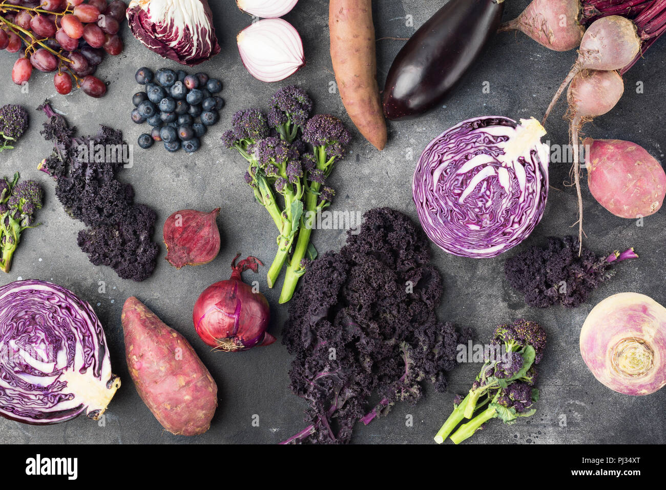 Fruits et légumes contexte en violet, vert et rouge foncé, le chou kale couleurs de pommes de terre choux brocolis oignons raisins bleuets, vue du dessus, fond gris foncé, selective focus Banque D'Images