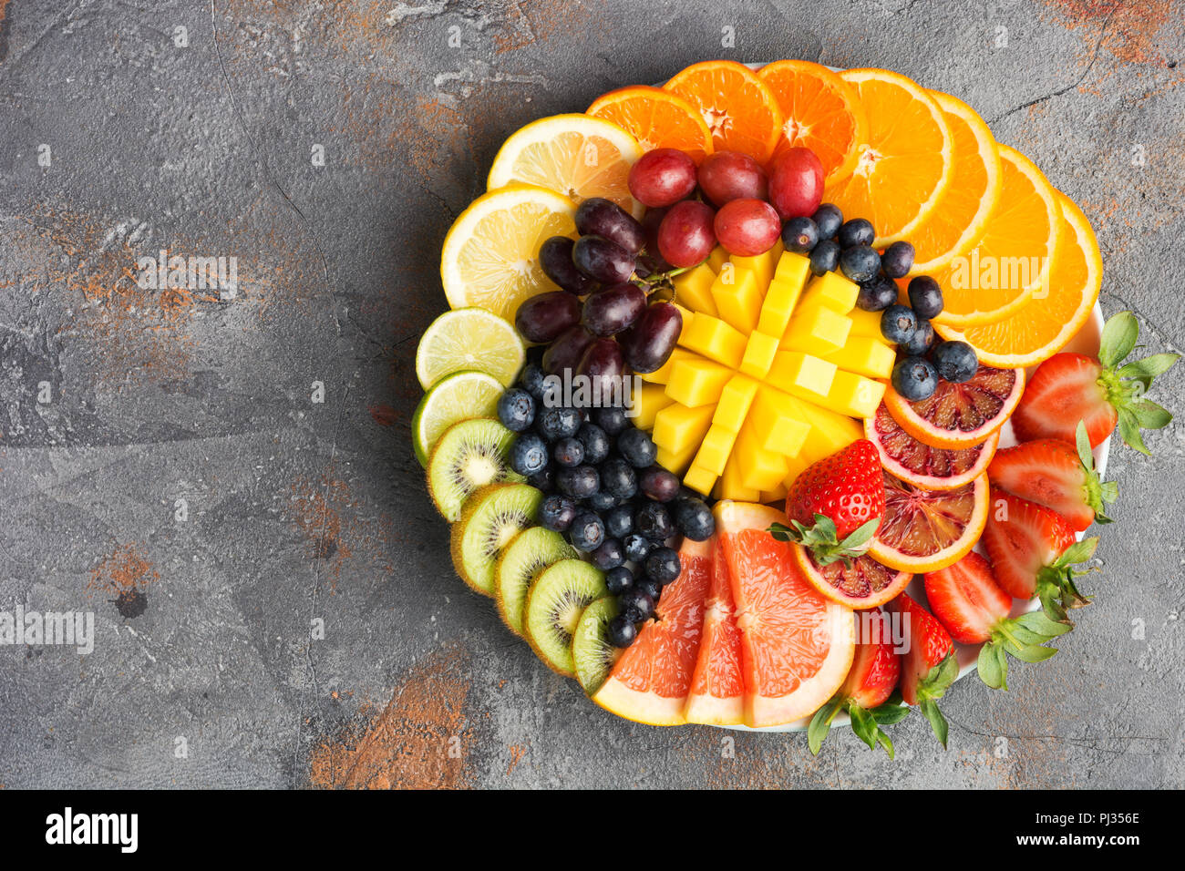 Assortiment de fruits coupés en couleurs arc-en-ciel raisins oranges fraises kiwis mangue pamplemousses sur les bleuets la table de béton gris, vue du dessus, copiez l'espace, selective focus Banque D'Images