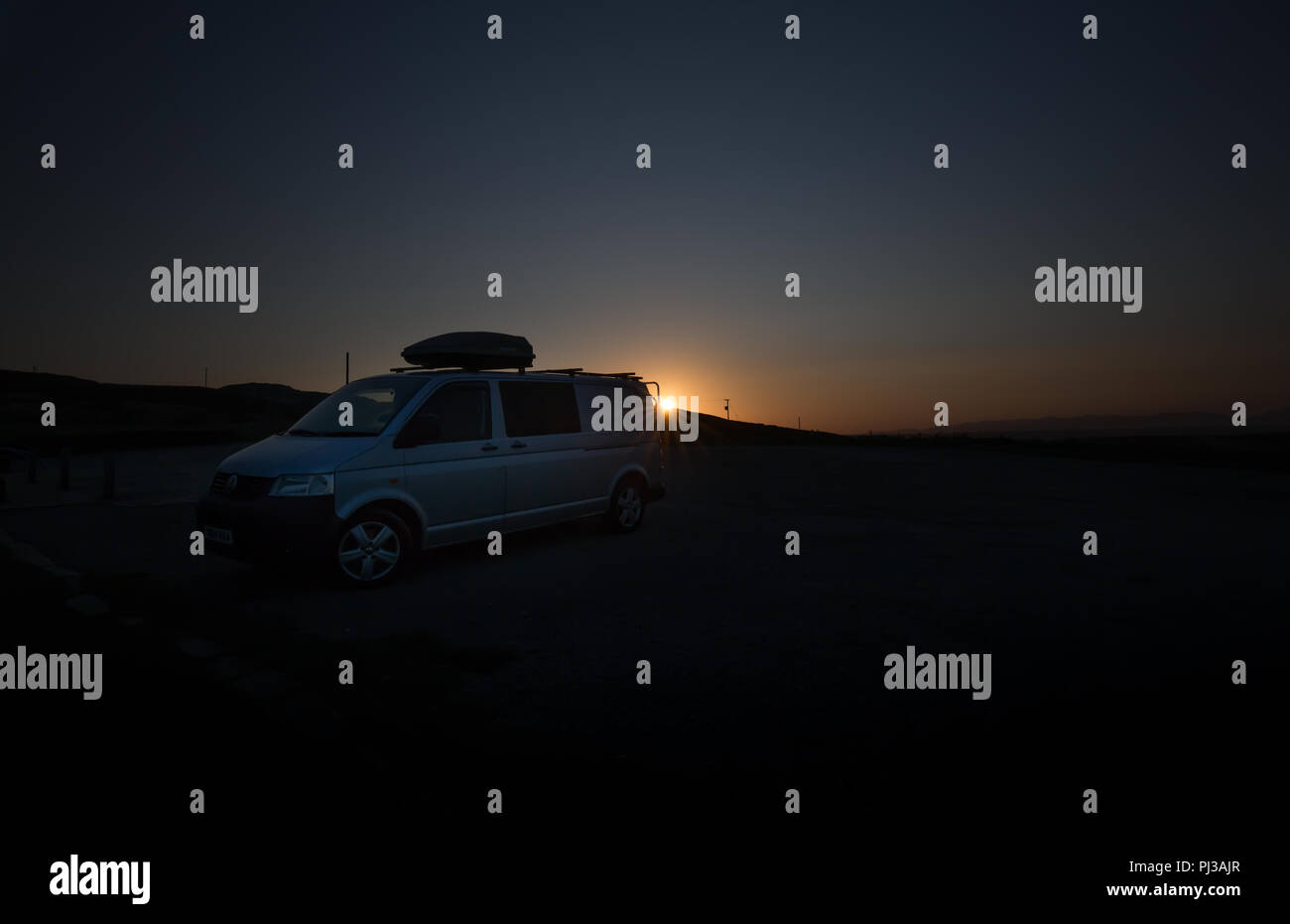 Vue de côté de l'argent VW Transporter T5 campervan (&) qui se profile au lever du soleil. Vue de l'atmosphère ; la première lumière magique ; lever de soleil, UK campagne. Banque D'Images