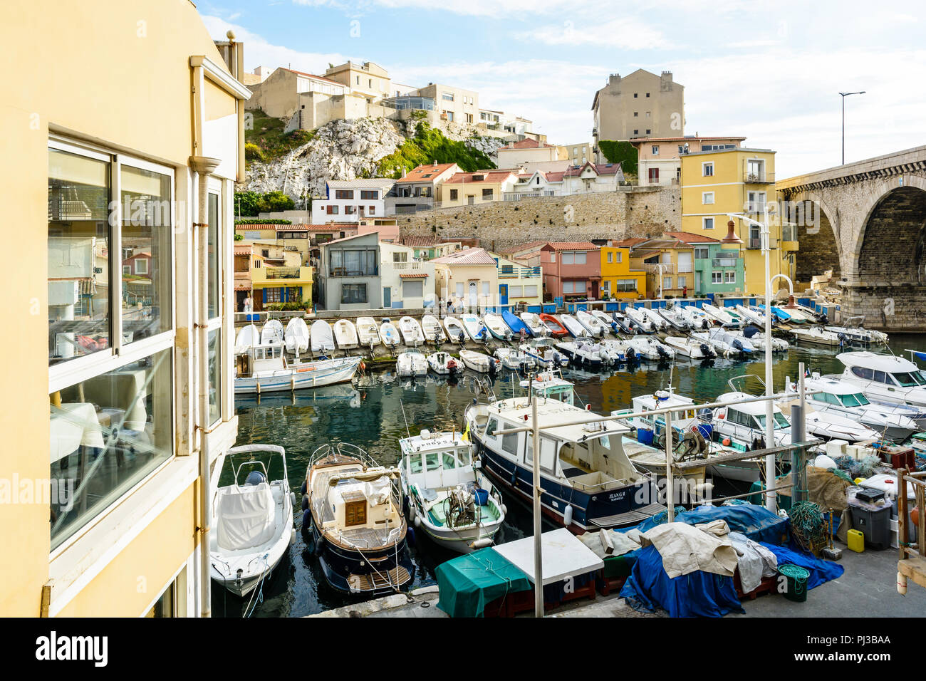 Le petit port du Vallon des Auffes à Marseille avec ses bateaux amarrés devant les maisons et cabanons colorés au-dessous du pont routier et de la falaise. Banque D'Images