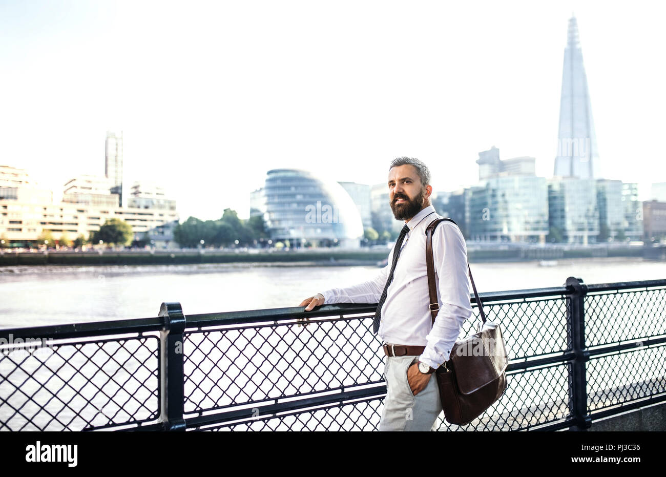 Homme d'Hipster avec sac pour ordinateur portable debout près de la rivière à Londres. Banque D'Images