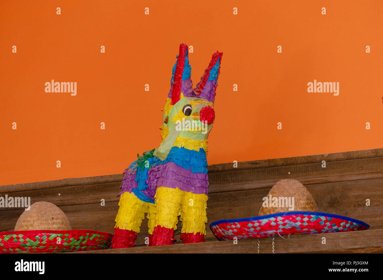 Piñata colorées et de chapeaux sur présentoir monté sur mur orange. Banque D'Images