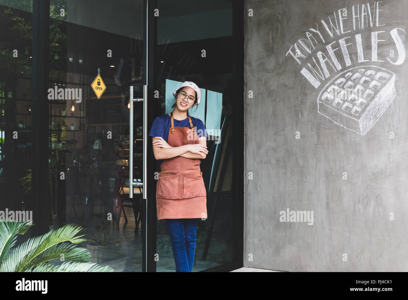 Portrait of smiling young woman with arms crossed standing at coffee shop Banque D'Images