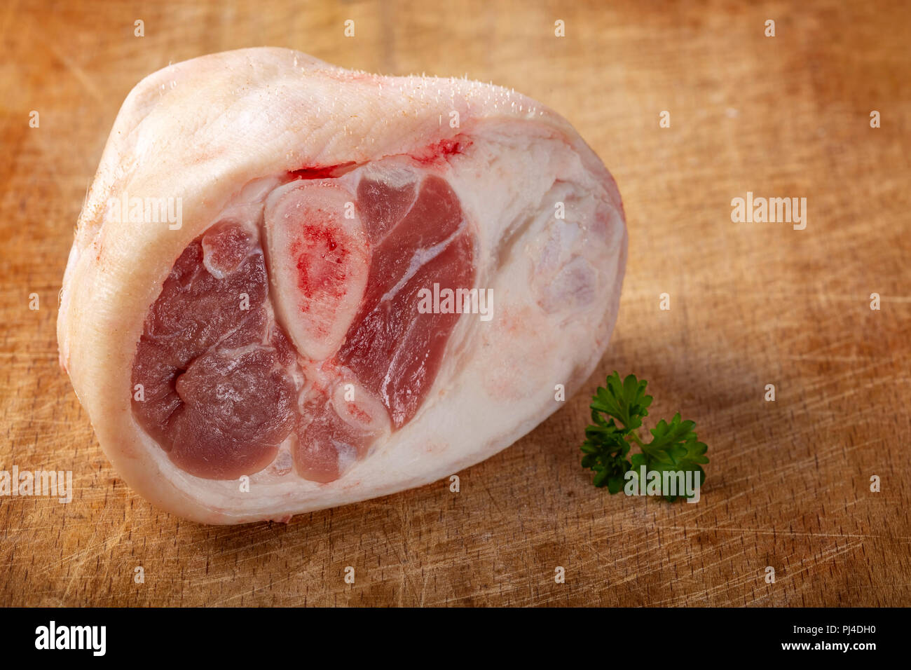 Morceau de jarret de porc crus avec des feuilles de persil sur fond de bois Banque D'Images