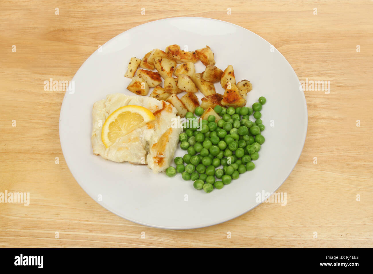 Cabillaud poêlé aux pommes de terre et les pois sur une plaque sur une table en bois Banque D'Images