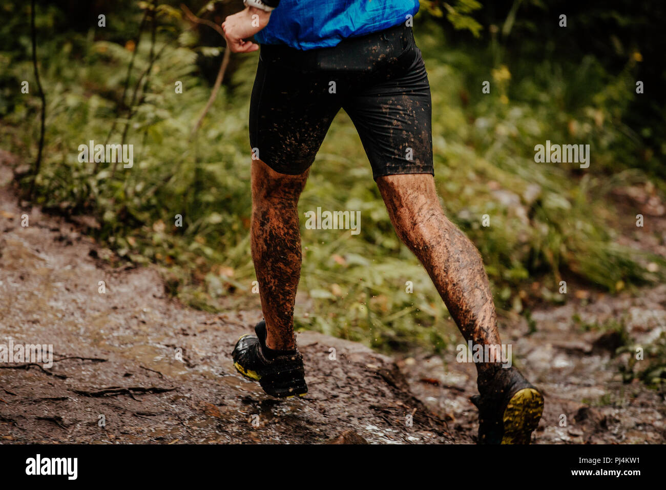 Retour homme runner dans la boue s'exécutant sur sentier en forêt d'automne Banque D'Images