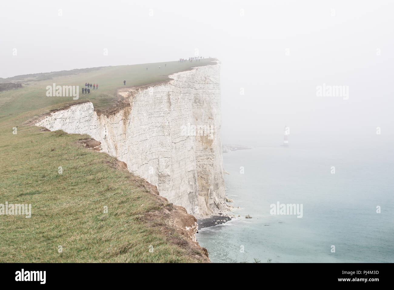 Phare dans la brume, grande falaise, à distance et les oiseaux jouer et voler librement sous la falaise. Petite silhouette d'un homme escalade la falaise. Beachy H Banque D'Images