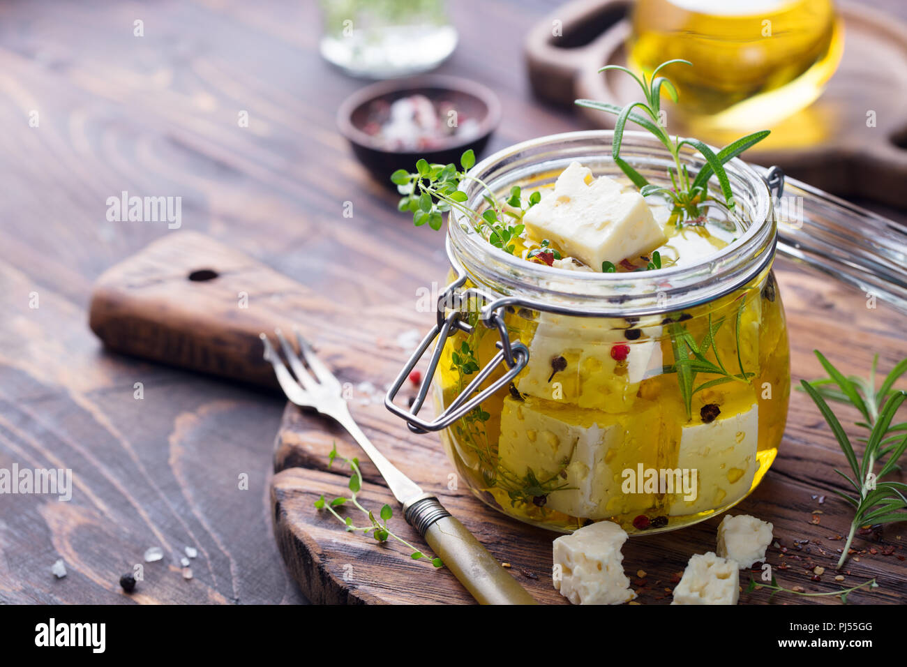 Le fromage Feta mariné à l'huile d'olive avec des herbes fraîches dans un bocal en verre. Fond de bois. Copier l'espace. Banque D'Images