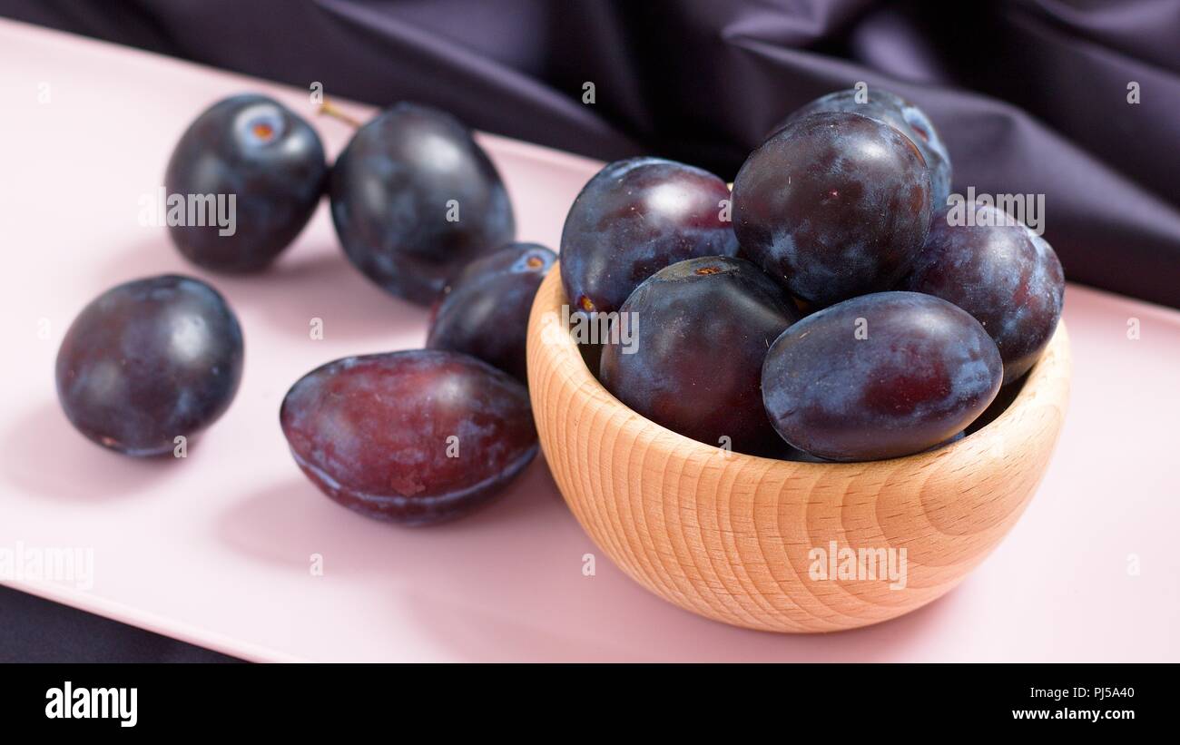 Sweet Ripe purple prunes dans bol en bois sur plateau rose Banque D'Images