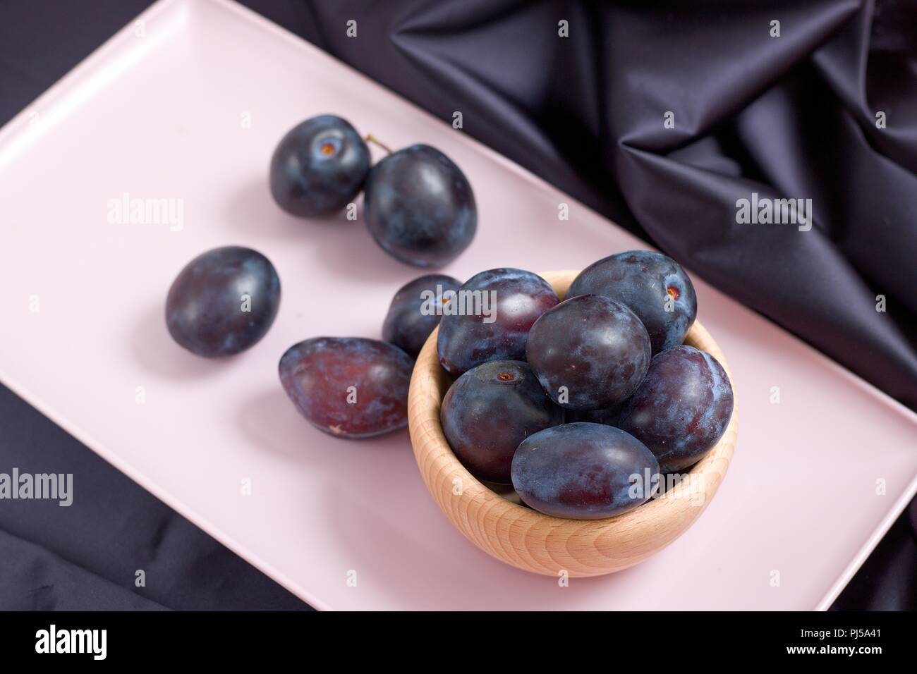 Snack-naturels sains. Les prunes violettes mûres dans bol en bois sur plateau rose Banque D'Images