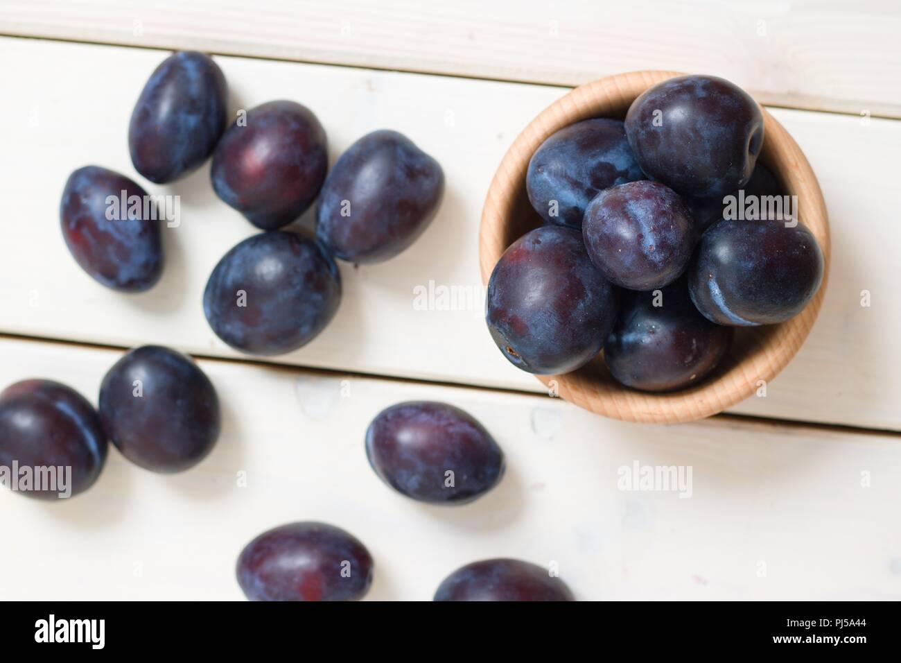 Vue du haut vers le bas sur les prunes dans bol en bois bleu et blanc renversé autour sur table en bois Banque D'Images