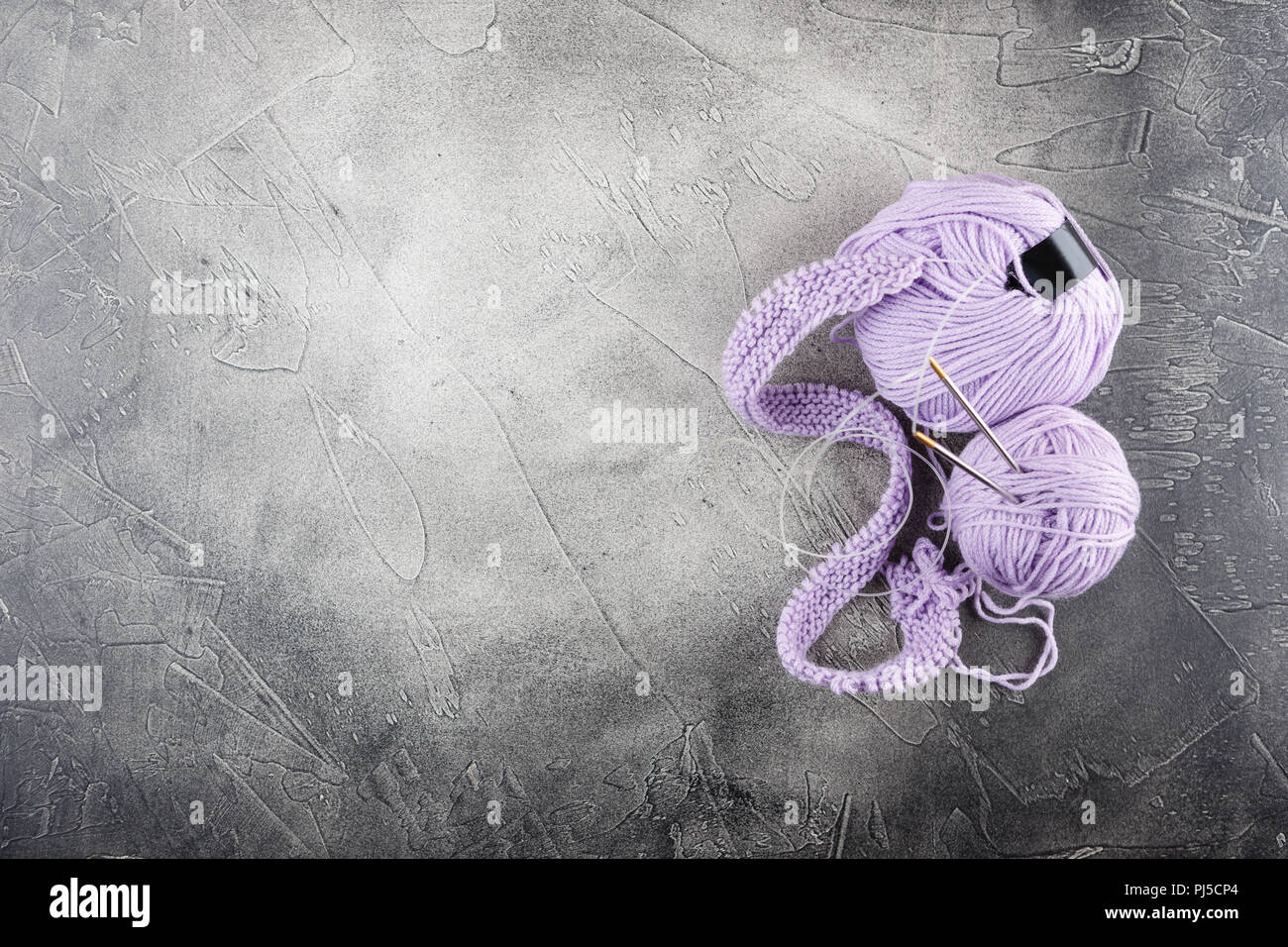 Hanks de lilas, fils de laine et aiguilles à tricoter un motif sur fond gris Banque D'Images