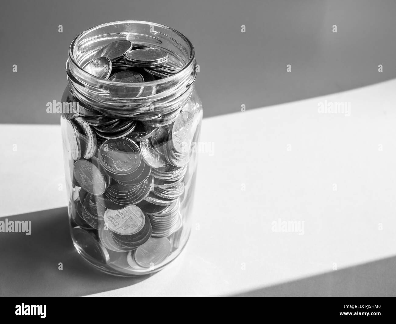 Pièces de monnaie dans un bocal en verre isolé sur fond bleu avec l'espace de copie en noir et blanc de style. Concept d'économiser de l'argent. Banque D'Images
