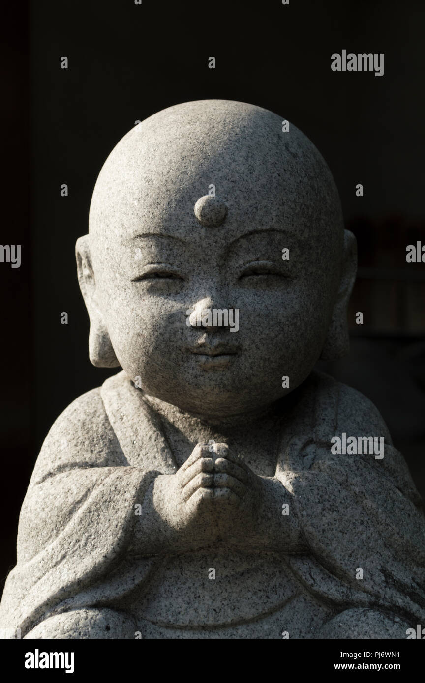 Cute Little Buddha statue de pierre prier et souriant avec les yeux fermés. Banque D'Images