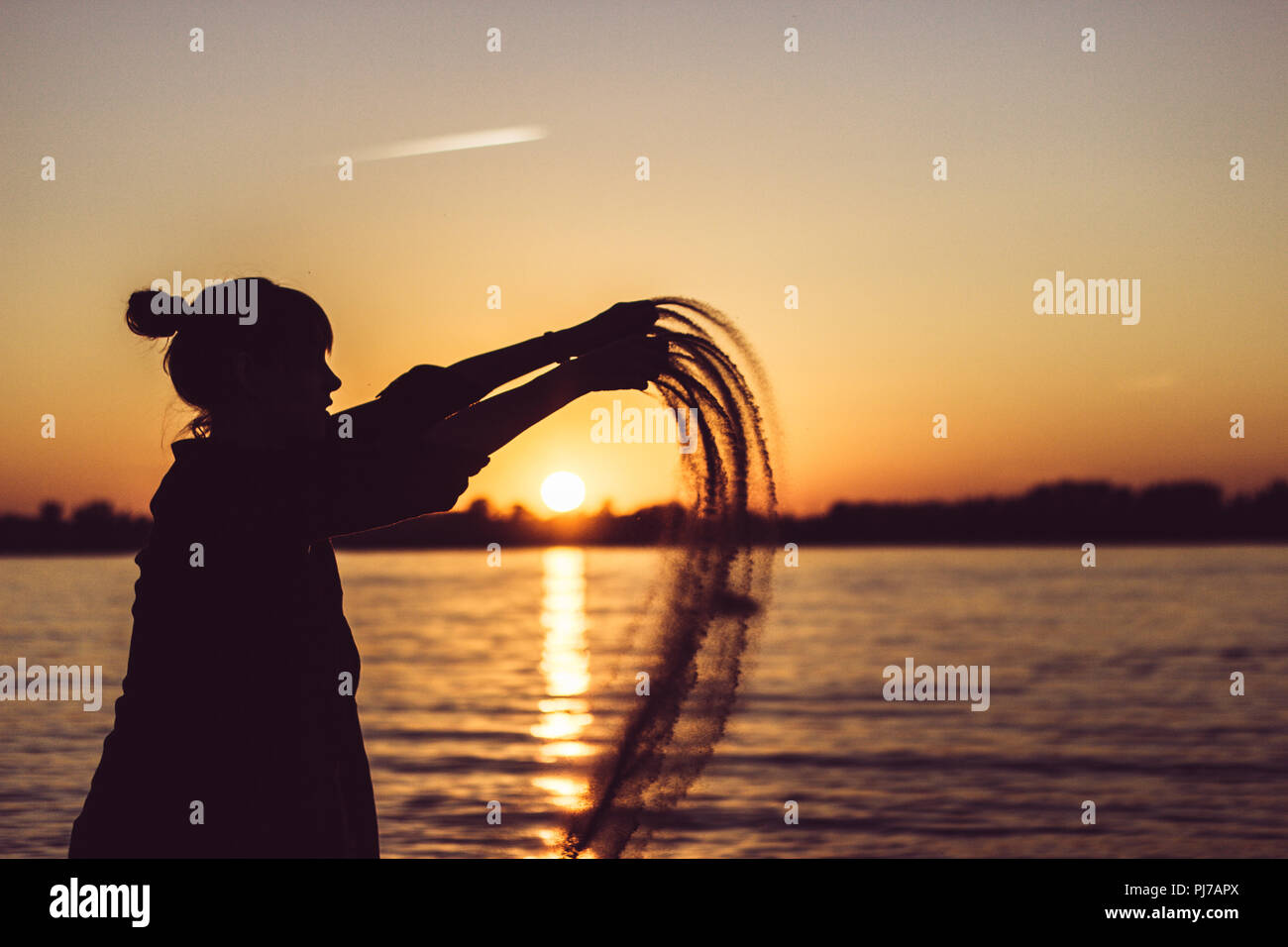 Femme jouant avec le sable sur la plage au coucher du soleil Banque D'Images
