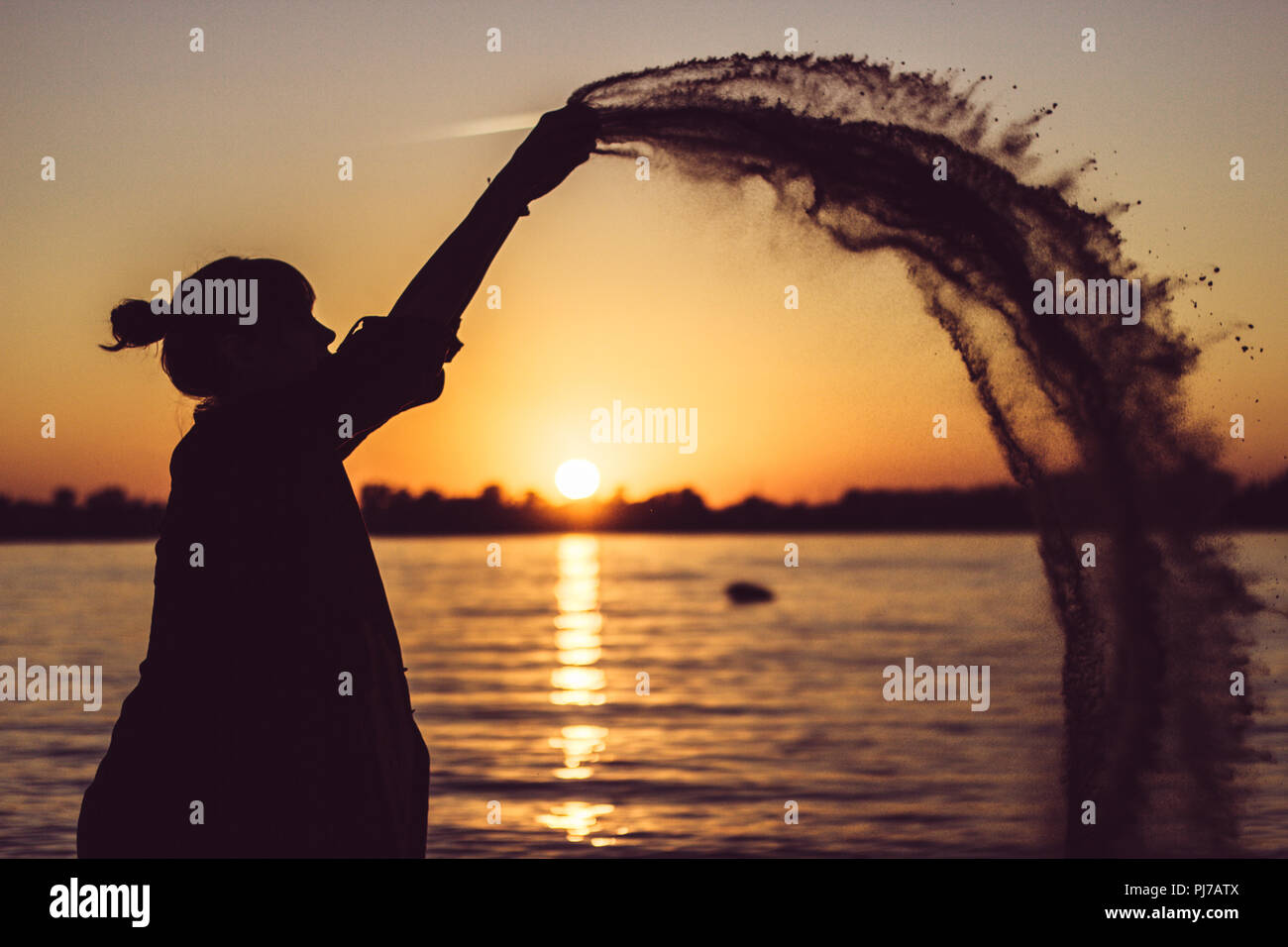 Femme jouant avec le sable sur la plage au coucher du soleil Banque D'Images