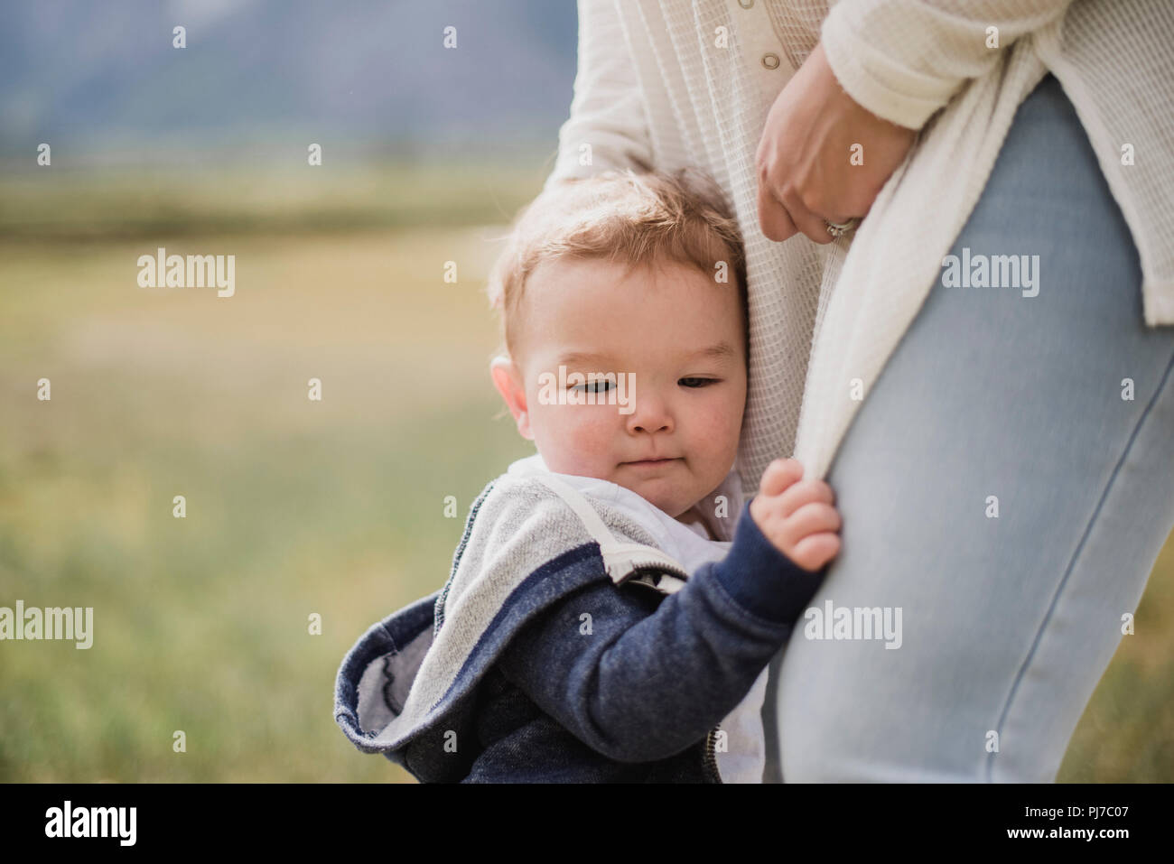 Bébé fils affectueux de la mère s'accroche à jambes Banque D'Images