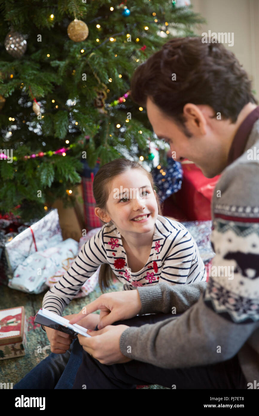Père reading book with daughter at Christmas Tree Banque D'Images