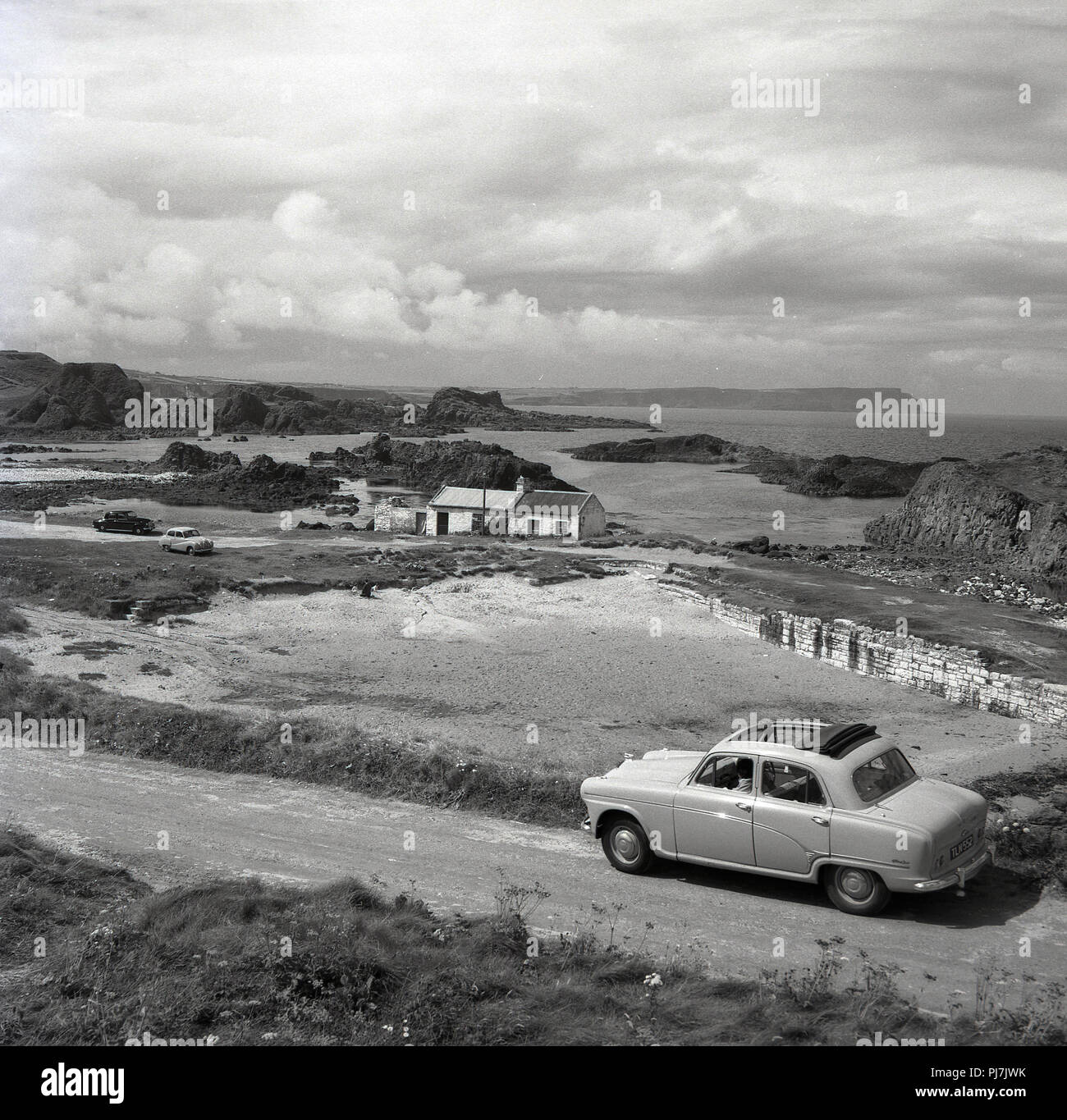 Années 1950, historique photo od une voiture garée par une charmante baie déserte sur la côte d'Antrim, Irlande du Nord, Royaume-Uni > Banque D'Images
