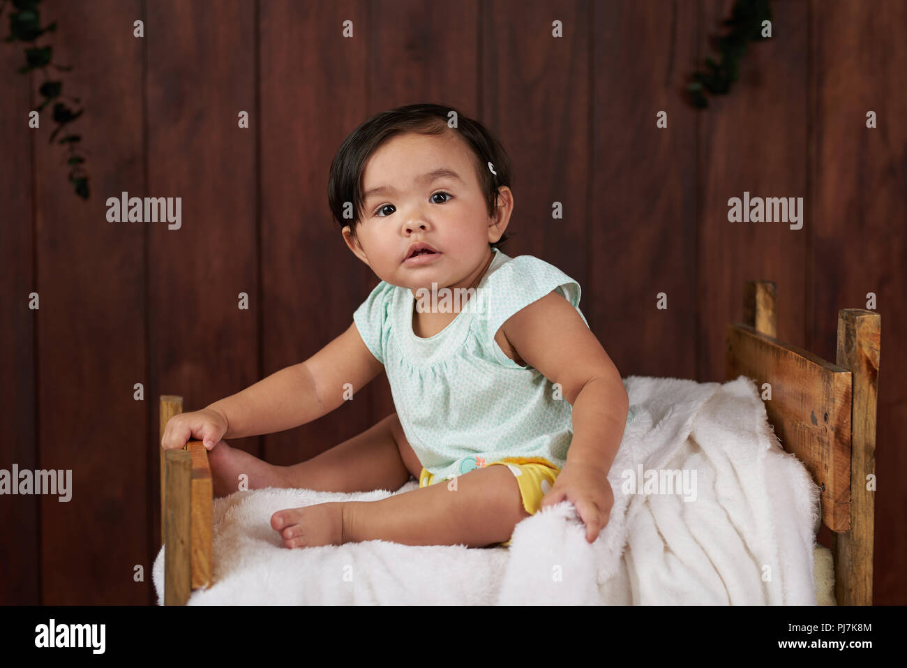 Baby Girl s'asseoir sur le lit en bois sombre sur fond de studio Banque D'Images