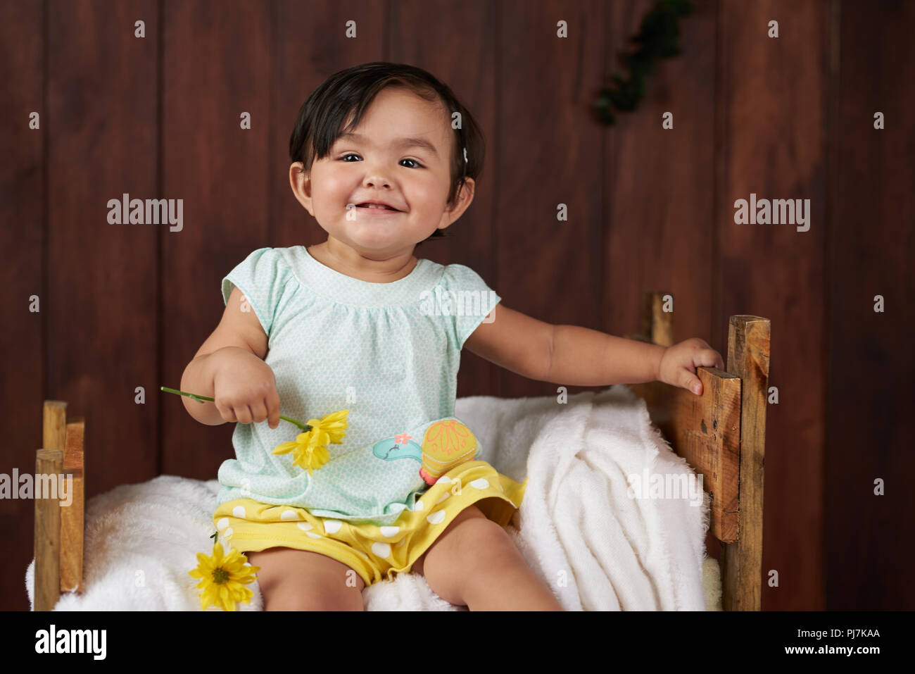 Jolie petite fille avec une fleur dans la main sur fond de bois brun Banque D'Images
