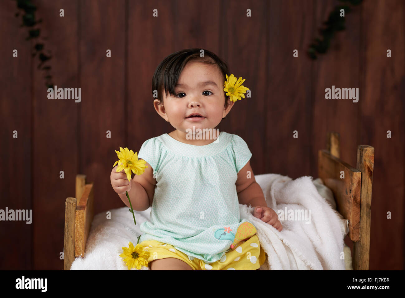 Baby Girl avec fleur jaune, s'asseoir sur le lit avec fond de bois Banque D'Images