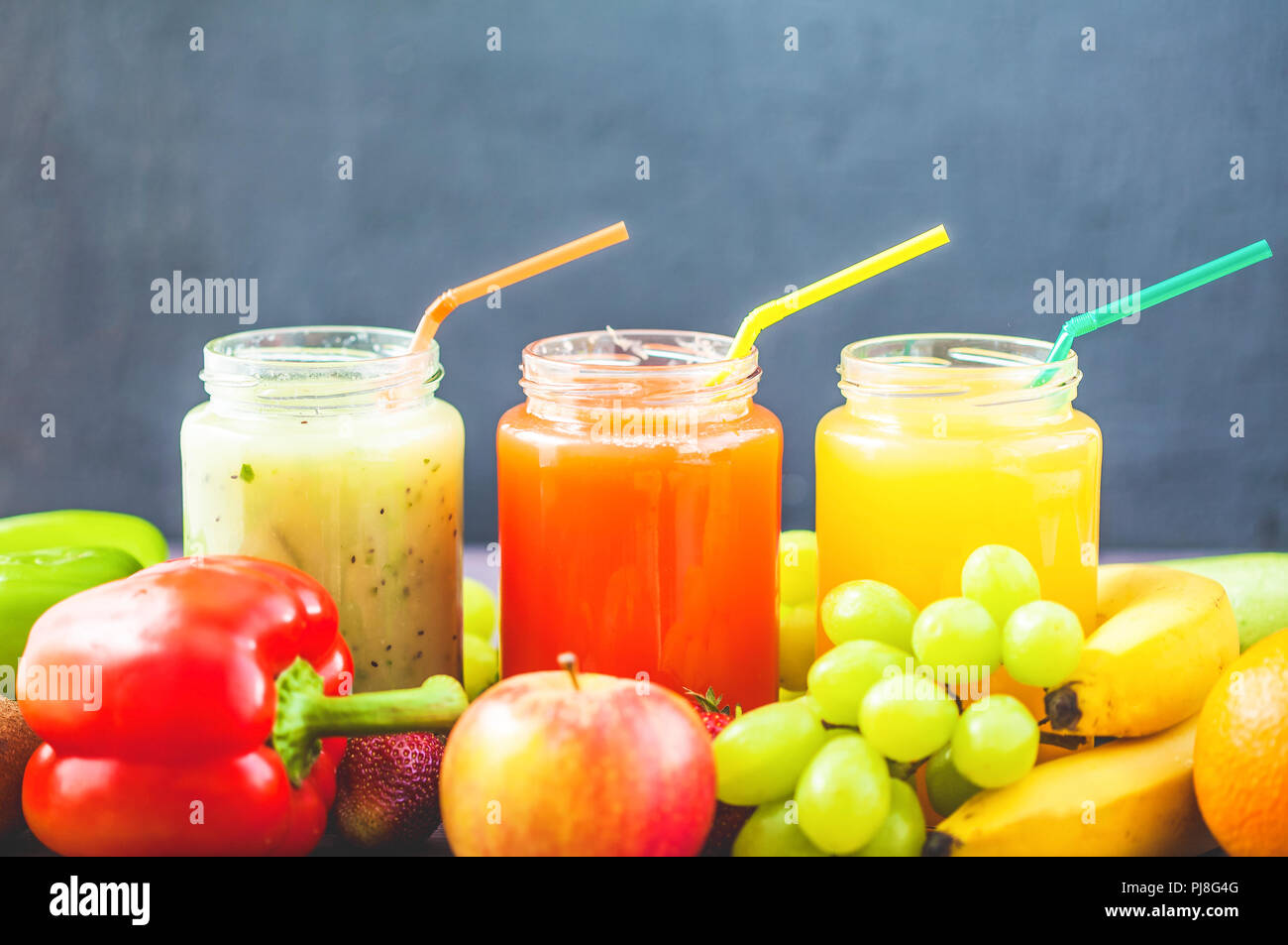Jus de fruits fraîchement pressés, des smoothies banane citron vert orange jaune pomme orange kiwi fraise raisin sur un fond de bois foncé Copy space Banque D'Images
