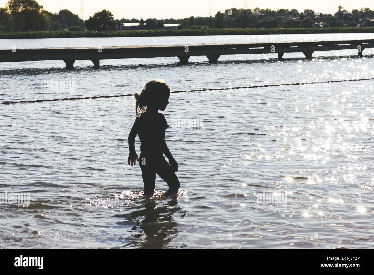 Petite fille qui marche dans l'eau peu profonde dans le coucher du soleil Banque D'Images