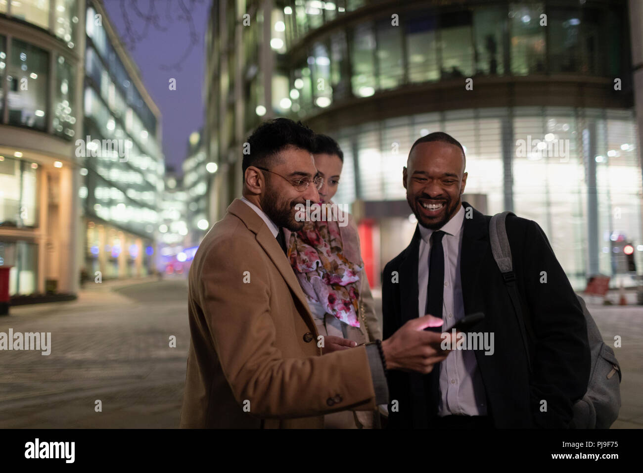 Les gens d'affaires à l'aide de smart phone on urban street at night Banque D'Images