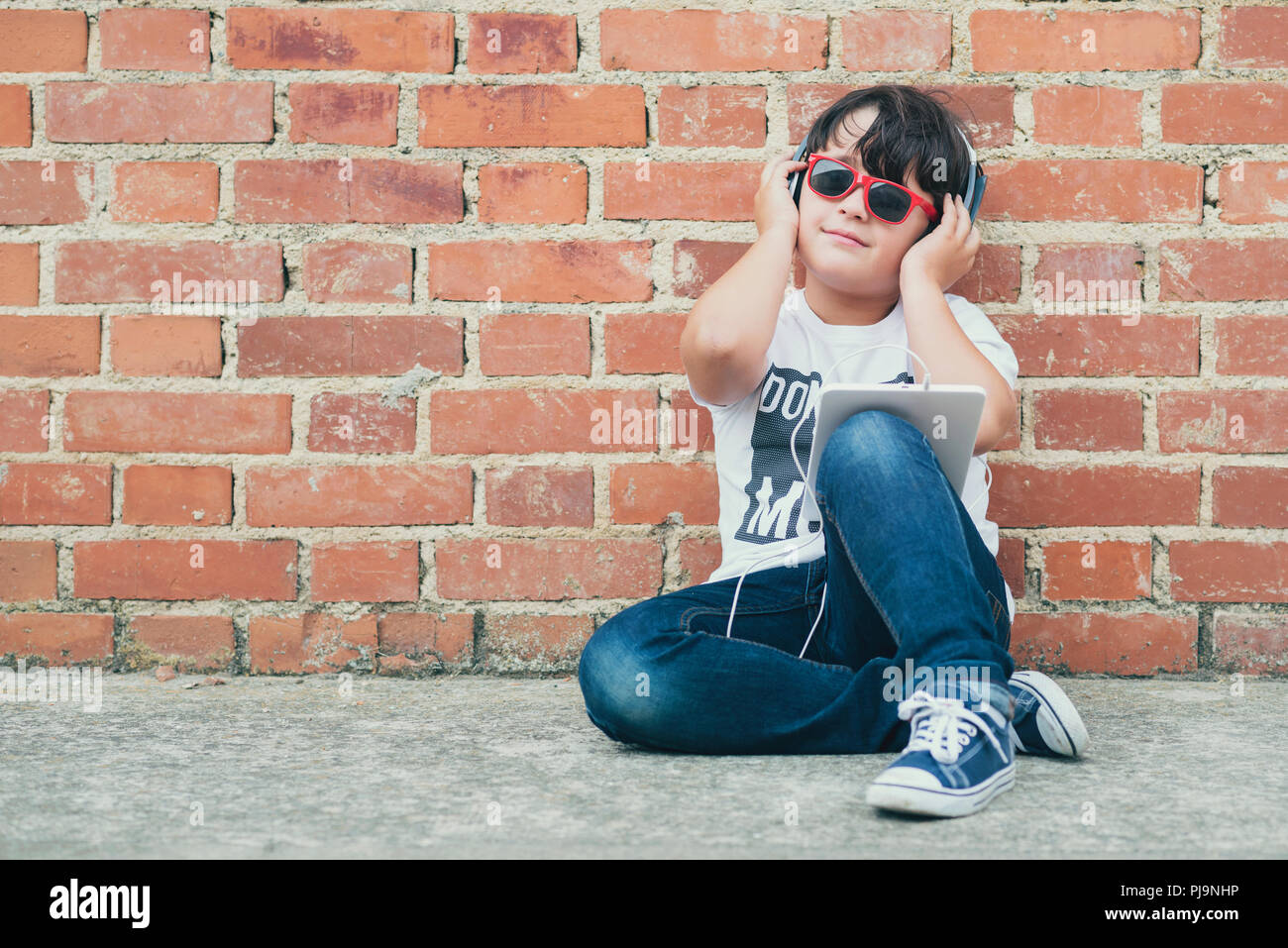 Enfant avec casque connecté avec tablette numérique assis sur le plancher Banque D'Images