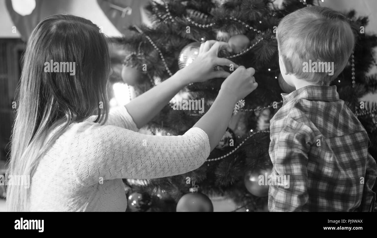 Portrait noir et blanc de petit bébé garçon à la mère à ornant Christmas Tree in living room Banque D'Images