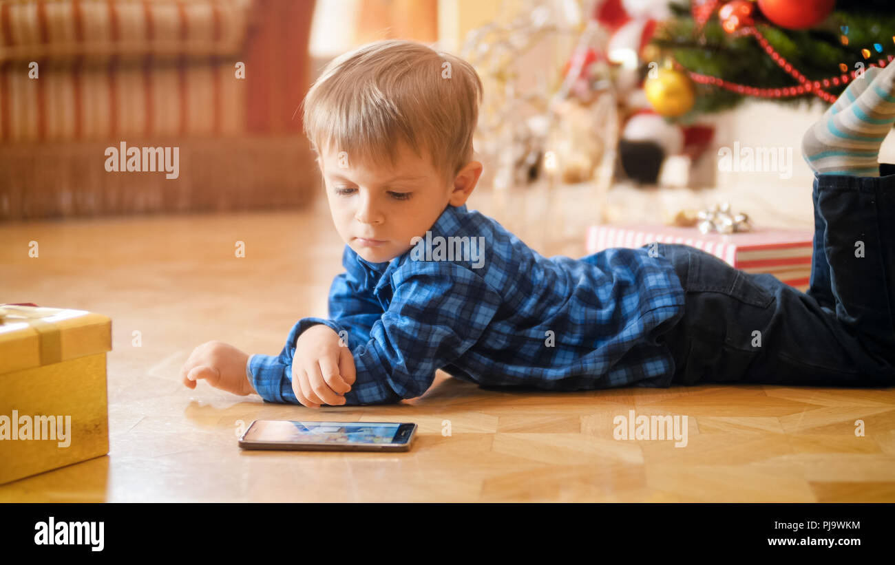 Cute 3 Ans Bebe Garcon Couche Sous L Arbre De Noel Et Regarder Les Dessins Animes Sur Telephone Mobile Photo Stock Alamy