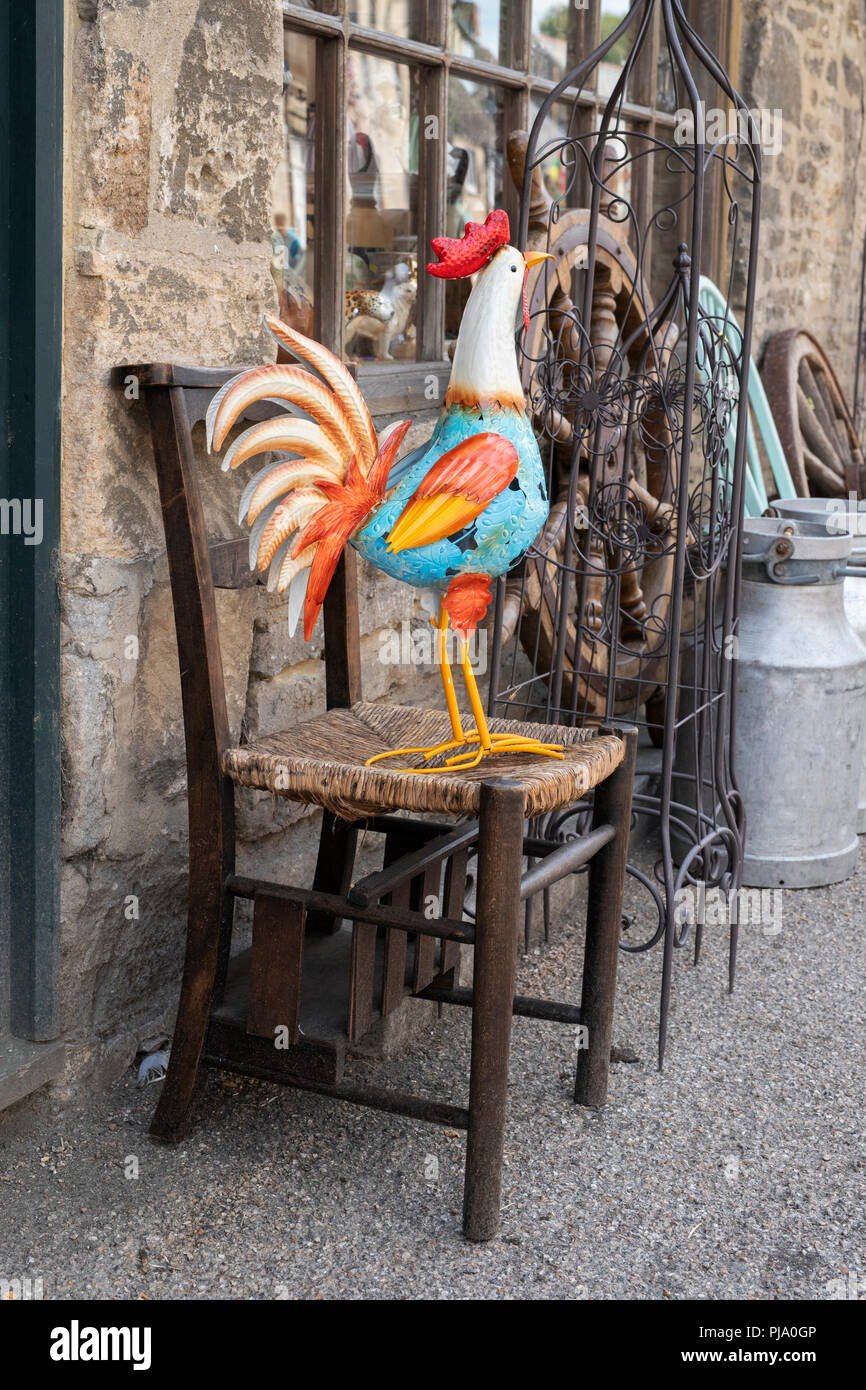 Coq en métal coloré sur une chaise en bois à l'extérieur et boutique d'antiquités à Lechlade on Thames, Gloucestershire, Angleterre Banque D'Images