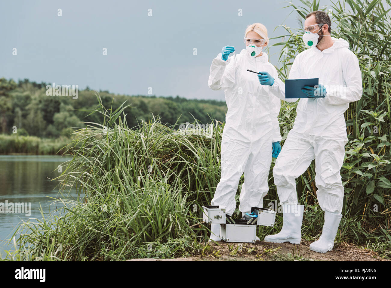 Homme libre de masque et écrit dans le presse-papiers et de pointage pendant que son collègue de l'échantillon de l'examen de l'eau dans la fiole de test pis Banque D'Images