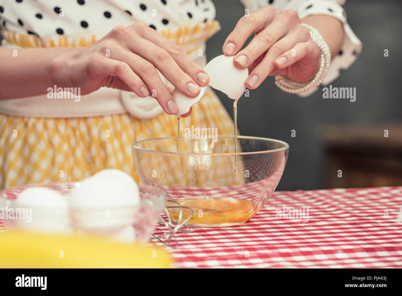Cropped shot de femme au foyer dans la chemise à pois casser oeuf en omelette pour bol Banque D'Images
