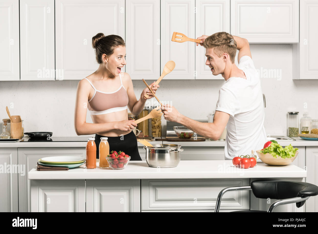 Jeune couple se battre avec spatules en bois dans la cuisine Banque D'Images