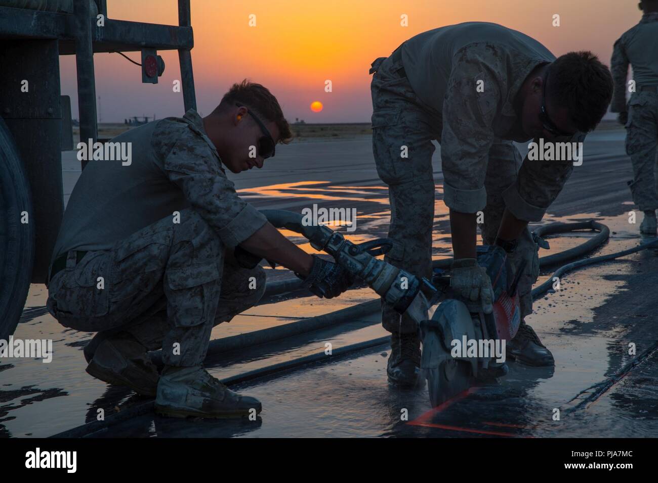 Lieu inconnu, au Moyen-Orient - U.S. Marine Corps Cpl. Joshua Garza (à gauche), un technicien en réparation de petit calibre, et Connor LCpl Reid (à droite), ingénieur de combat avec l'Escadron de soutien de l'aile Marine 371 joint à but spécial air-sol marin crise Response-Central, Groupe de travail de commande pour réparer un trottoir endommagé le 3 juillet 2018, l'aérodrome. L'équipe de réparation des dommages de l'aérodrome assure pistes sont sûr à mener des opérations de vol dans toute la région. Banque D'Images
