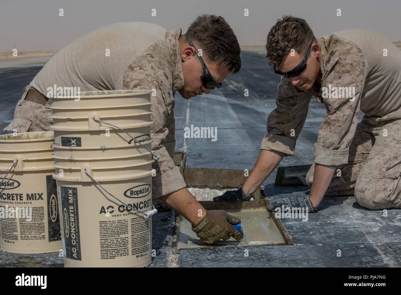 Lieu inconnu, au Moyen-Orient - U.S. Marine Corps Cpl. Joseph Dudley (à gauche), un administrateur des systèmes de données et le Cpl. Joshua Garza (à droite), un technicien en réparation de petit calibre avec l'Escadron de soutien de l'aile Marine 371 joint à but spécial du Groupe de travail air-sol marin, de crise Response-Central béton lisse commande alors que la réparation d'un aérodrome endommagé le 3 juillet 2018. L'équipe de réparation des dommages de l'aérodrome assure pistes sont sûr à mener des opérations de vol dans toute la région. Banque D'Images