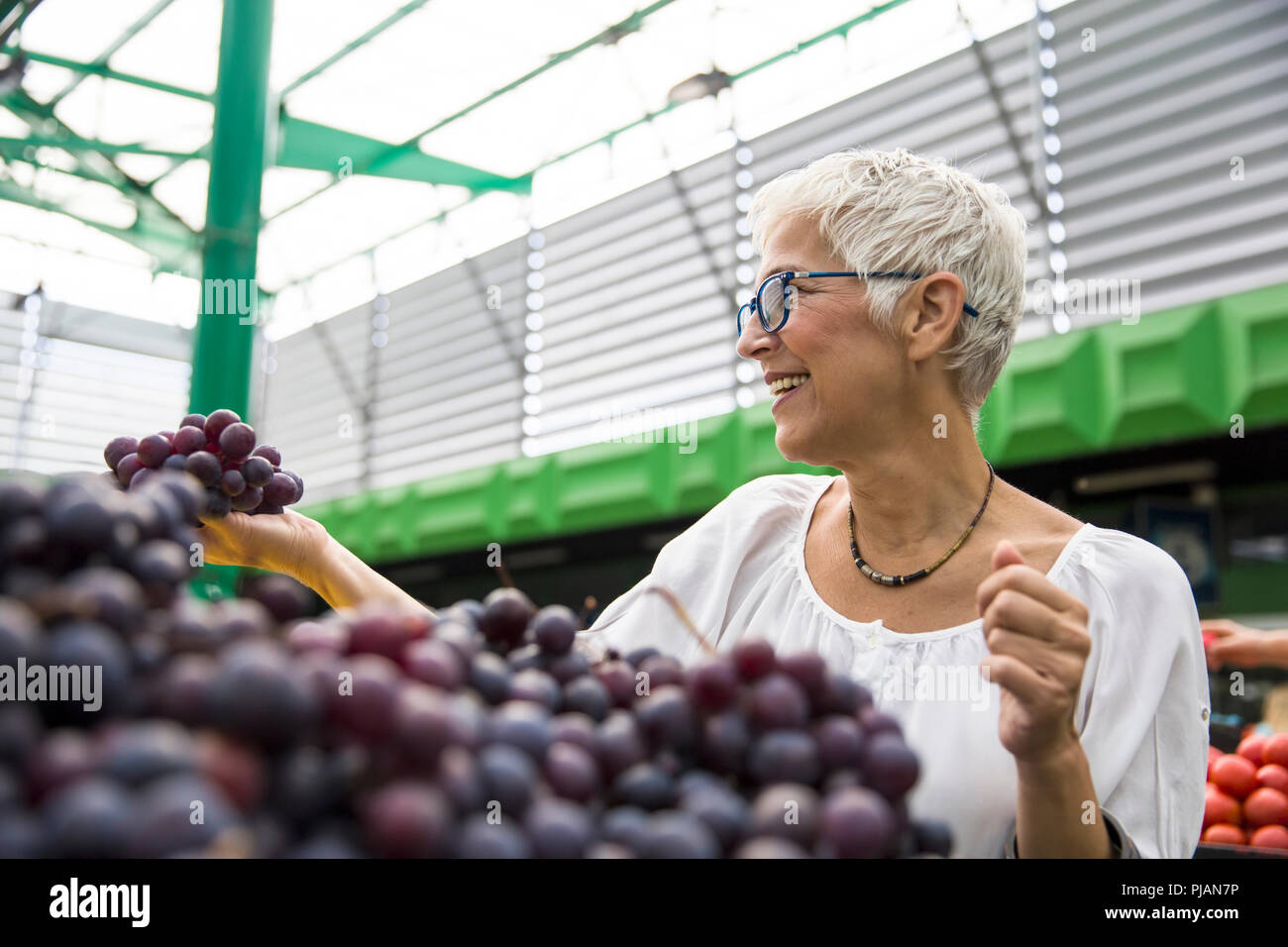 Portrait of senior femme choisit de raisins rouges au marché Banque D'Images