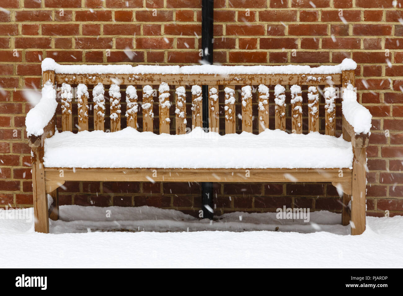 Banc de jardin en bois recouvert de neige contre un mur de briques Banque D'Images