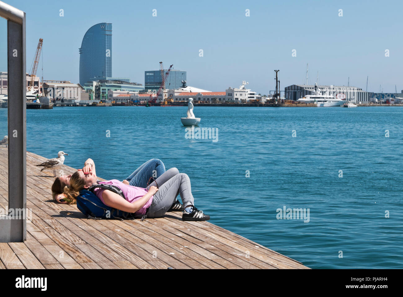 Deux jeunes femmes se trouvant sur le plancher en bois par le bord de la jetée du Port Vell, Barcelone, Espagne Banque D'Images