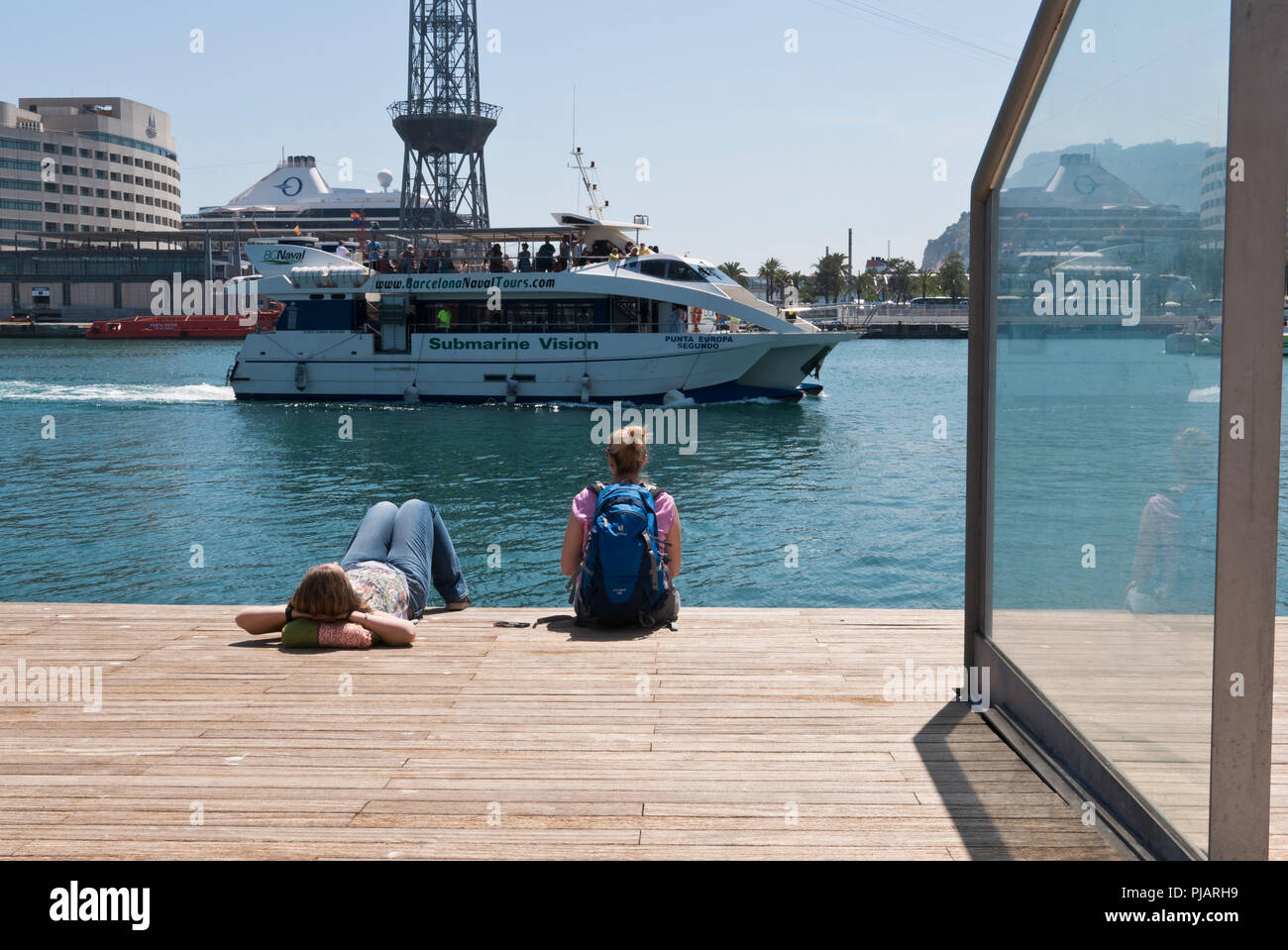 Deux jeunes femmes de l'emplacement sur le plancher en bois au bord de la jetée du Port Vell et regarder un bateau passant par, Barcelone, Espagne Banque D'Images