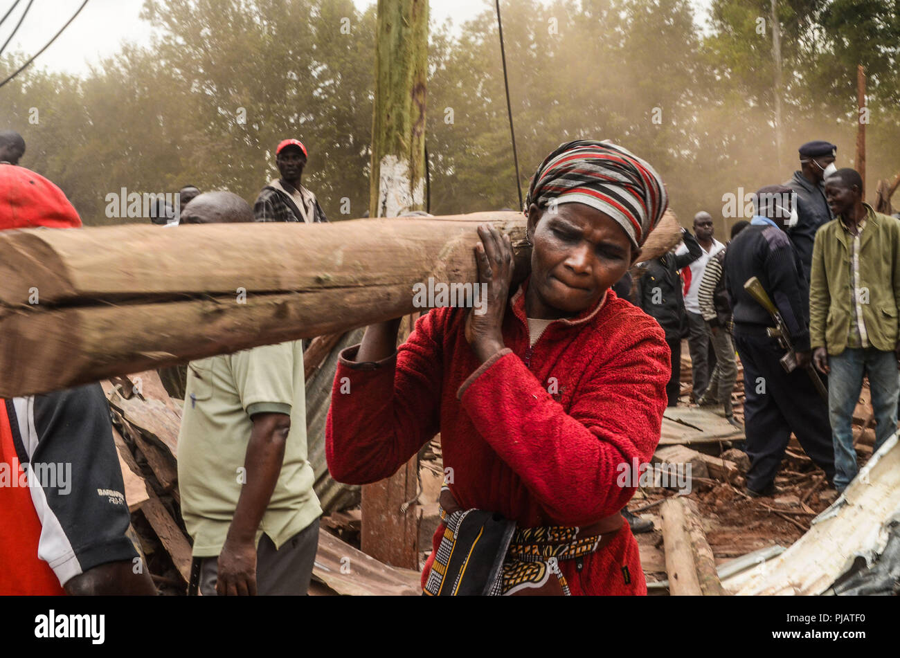 Une femme vu porter un énorme log pendant la démolition. La démolition par le gouvernement pour créer les routes et faciliter la congestion du trafic autour de Nairobi a fait plus de vingt mille familles sans abri dans les bidonvilles de Kibera. La situation a également touché certaines organisations non gouvernementales et les écoles privées autour de la zone. Banque D'Images