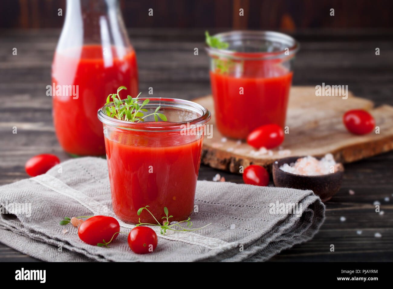 Du jus de tomate dans du verre, avec salade de cresson, tomates fraîches sur planche à découper en bois et gris serviette. Banque D'Images