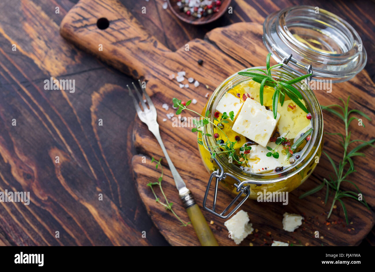 Le fromage Feta mariné à l'huile d'olive avec des herbes fraîches dans un bocal en verre. Fond de bois. Vue d'en haut. Copier l'espace. Banque D'Images