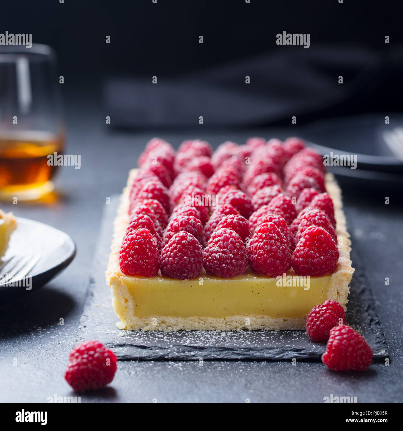 Tarte aux framboises avec la crème vanille et chocolat blanc sur ardoise. Arrière-plan de la pierre noire. Copier l'espace. Banque D'Images