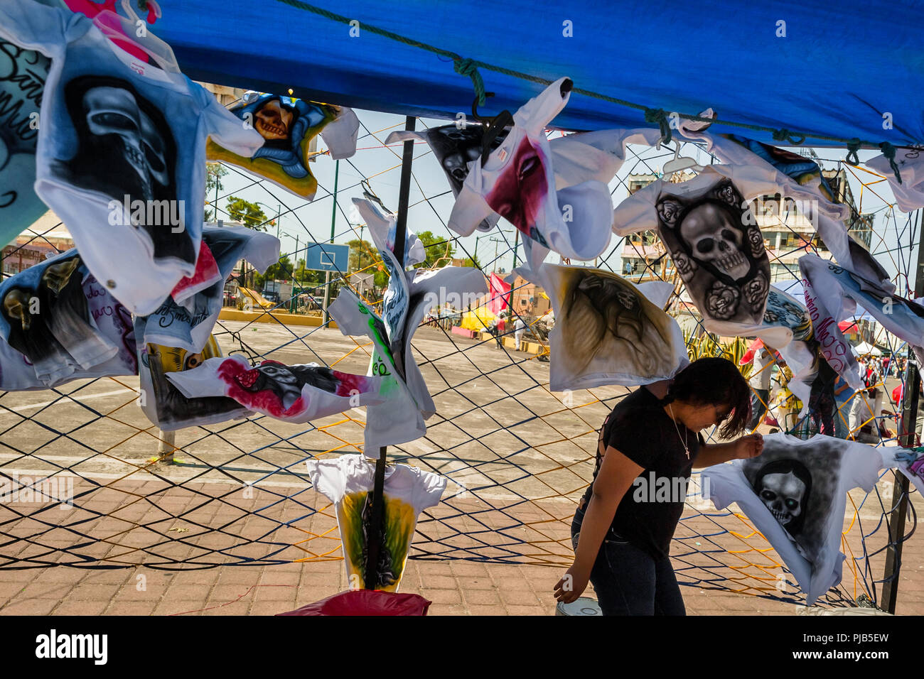 Une jeune femme mexicaine vend des t-shirts, avec divers Santa Muerte (sainte mort) images, dans la rue au cours d'un pèlerinage dans la ville de Mexico, Mexique. Banque D'Images