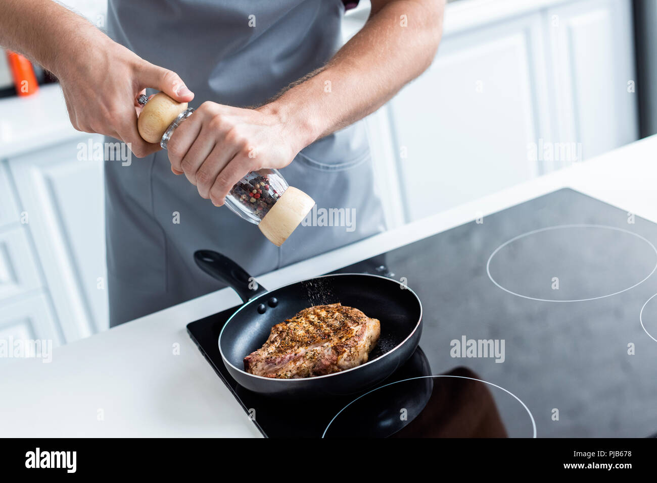 Cropped shot of man holding moulin à poivre pendant la cuisson des steaks délicieux dans une poêle Banque D'Images